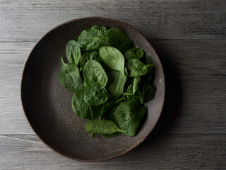 Top view of a rustic dark plate isolated with fresh spinach leaves on dark wooden table. Healthy...