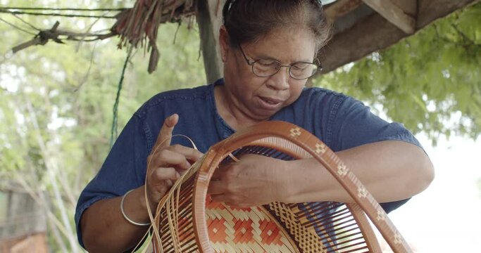 Old Thai female farmer weave baskets in traditional Thai art patterns to sell as extra income in countryside of Thailand.
