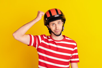Photo of funny unsure young guy dressed red t-shirt hands arm fist safety hat isolated yellow color background