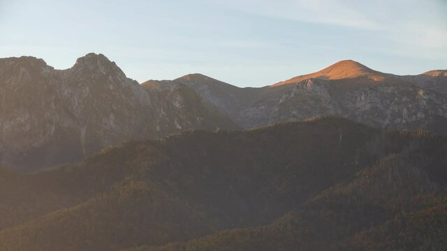 Time lapse shot mountains, peaks, mountain range lit with warm morning sun light. Epic rocky highlands and beautiful hills covered with pine trees forest sunrise time-lapse