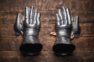 Metal knight gloves on the wooden brown flat lay table background.