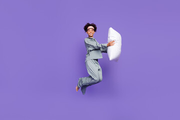 Photo of sweet beautiful woman grey sleepwear holding pillow jumping high smiling isolated violet...