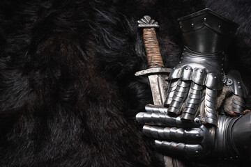 Knight sword and steel gloves on the black animal skin background.