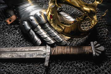 Knight sword and golden crown on the ancient table close up.