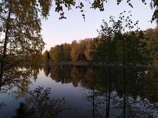 Fototapeta na wymiar Fall landscape with reflection of trees in the calm river water in sunny autumn evening