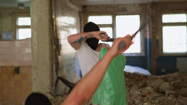 Killed criminal in mask falls down and scared companion tries to run away while hostage with plastic bag on head sits in abandoned building