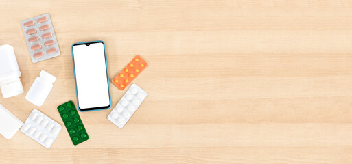 Smart phone with blank screen and pills, on wooden desktop. Top view.