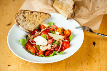Italian salad with tomato,onion, bacon and parmesan in white plate, fork, bread and paper.
