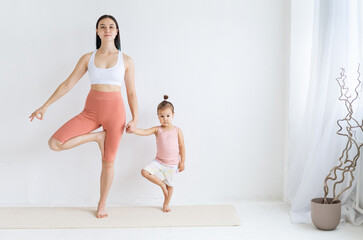 Young mother practices yoga with her daughter. Children's yoga. Vrikshasana pose. Couples yoga.