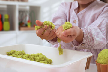 Little girl playing with bright kinetic sand at table indoors, closeup
