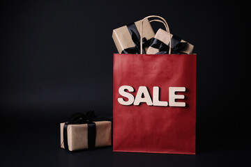 Red shopping bag with word Sale and gift boxes on dark background. Black Friday