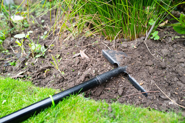 Steel half moon edger and spade seen in worked flowerbed soil.
