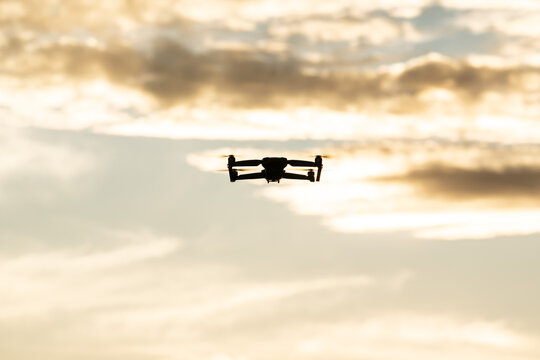Backlit silhouette of a four engine drone during an orange sunset with clouds