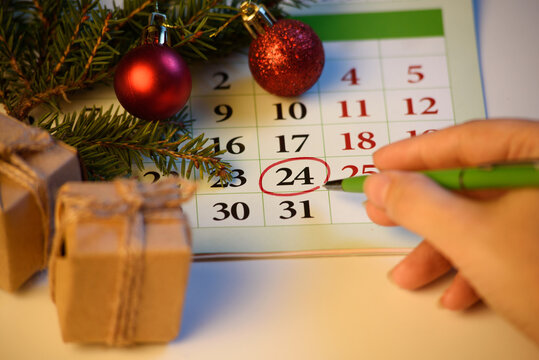 A woman's hand marks the date December 24 on the calendar. Preparing for christmas with spruce and new year decorations and gifts