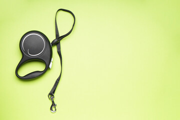 Black retractable dog leash on a green background, space for text. Flat lay.
