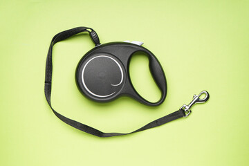Black retractable dog leash on a light green background, flat lay.