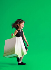 Girl in a black dress with paper bags goes shopping for discounts on a green background