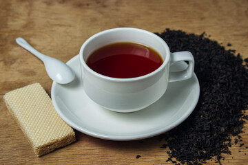 A cup of tea next to black loose tea. Cup of strong black tea on wooden background