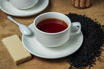 A cup of tea next to black loose tea. Cup of strong black tea on wooden background