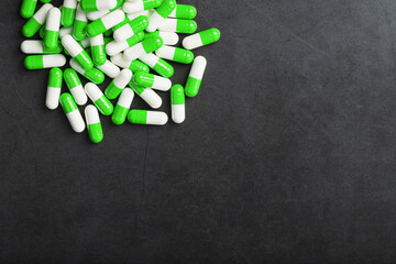 A handful of green and white pill capsules on a black background.
