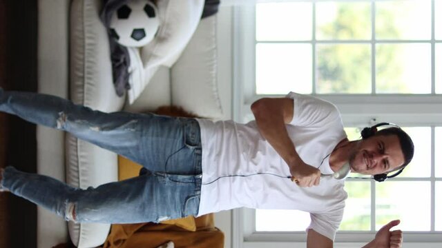 Cheerful man listening to music and dancing on soft couch at home in day off.