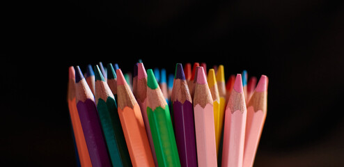 A closeup of the bunch of colored pencils on dark background.