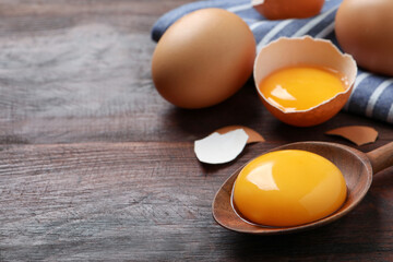 Spoon with raw egg yolk on wooden table, closeup. Space for text - obrazy, fototapety, plakaty