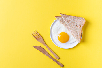 Fried egg and wholegrain bread toast in a white plate on a yellow background. Healthy breakfast. Top view
