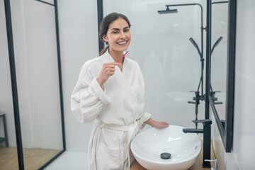 A woman in a white bath robe doing morning procedures in the bathroom