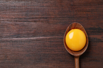 Spoon with raw egg yolk on wooden table, top view. Space for text - obrazy, fototapety, plakaty