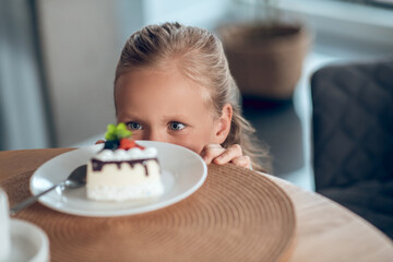 A cute blonde girl looking anticipated while looking at the slice of cake