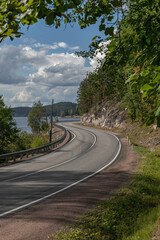 Fototapeta na wymiar Curve of an empty asphalt countryside highway. The road has 2 lanes, fenced and with white markings. Large stones, rocks and trees is on the side of the road, on the other side there is a Ladoga lake.