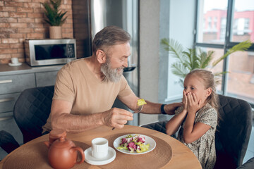 Family having breakfast together and dad trying to feed his daghter