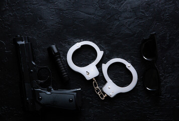 Black gun, flashlight, glasses and Police metal real handcuffs lie on the black background. Private detective work. Searching information. Crime and robbery, prison concept.