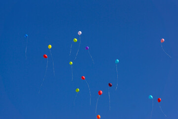 Bright inflatable balloons fly in the air against the backdrop of trees and blue sky during a festive holiday. Fireworks in the sky from colorful balloons.