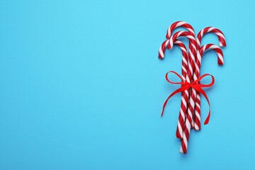 Sweet Christmas candy canes with red bow on light blue background, top view. Space for text