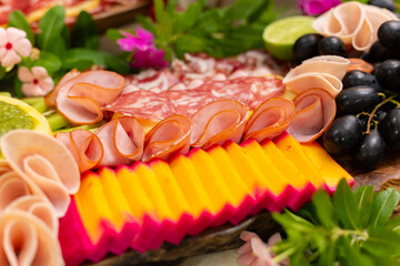 Detalhe de uma tábua de frios em cima da mesa, com salame, queijo, frutas.