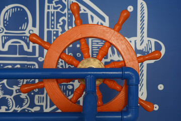 Photo of an orange steering wheel against a blue wall of a marine theme