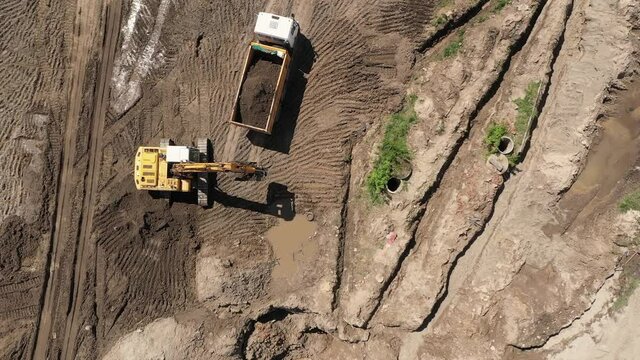 Industrial area from drone view. +Heavy equipment is grading the land, moving and flattening out red clay soil. Zoom out top down view of construction site with machinery, truck, excavator.
