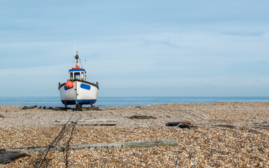 White and blue fishing boat park on rail track at a pebble beach at Dungeness, Kent, England