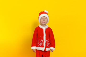 Handsome little boy stands on a yellow background dressed as Santa Claus and smiles cute.