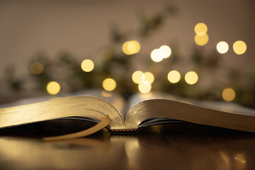open bible on wood table with golden christmas lights in background