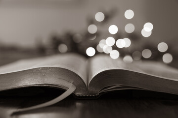 open bible on table with christmas lights in background