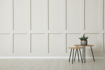 Tables with potted houseplant near empty wall indoors. Space for design