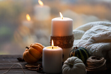 Autumn composition with candles, mini munchkin pumpkins, warm wool knitted plaid on the wooden wind sill. Dark colors, low key. Cozy home atmosphere, Thanksgiving decor, fall colors. Close up