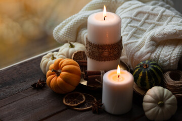 Autumn composition with candles, mini munchkin pumpkins, warm wool knitted plaid on the wooden wind sill. Dark colors, low key. Cozy home atmosphere, Thanksgiving decor, fall colors. Close up
