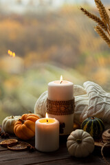 Autumn composition with candles, mini munchkin pumpkins, warm wool knitted plaid on the wooden wind sill. Dark colors, low key. Cozy home atmosphere, Thanksgiving decor, fall colors. Close up