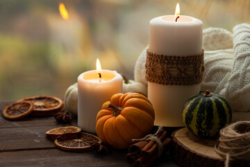 Obraz na płótnie Canvas Autumn composition with candles, mini munchkin pumpkins, warm wool knitted plaid on the wooden wind sill. Dark colors, low key. Cozy home atmosphere, Thanksgiving decor, fall colors. Close up