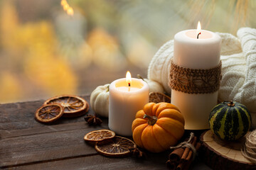 Autumn composition with candles, mini munchkin pumpkins, warm wool knitted plaid on the wooden wind sill. Dark colors, low key. Cozy home atmosphere, Thanksgiving decor, fall colors. Close up