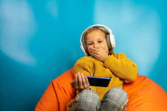 Closeup portrait anxious scared child blonde girl looking at phone seeing bad news photos message with disgusting emotion on her face isolated on blue background. Human reaction.